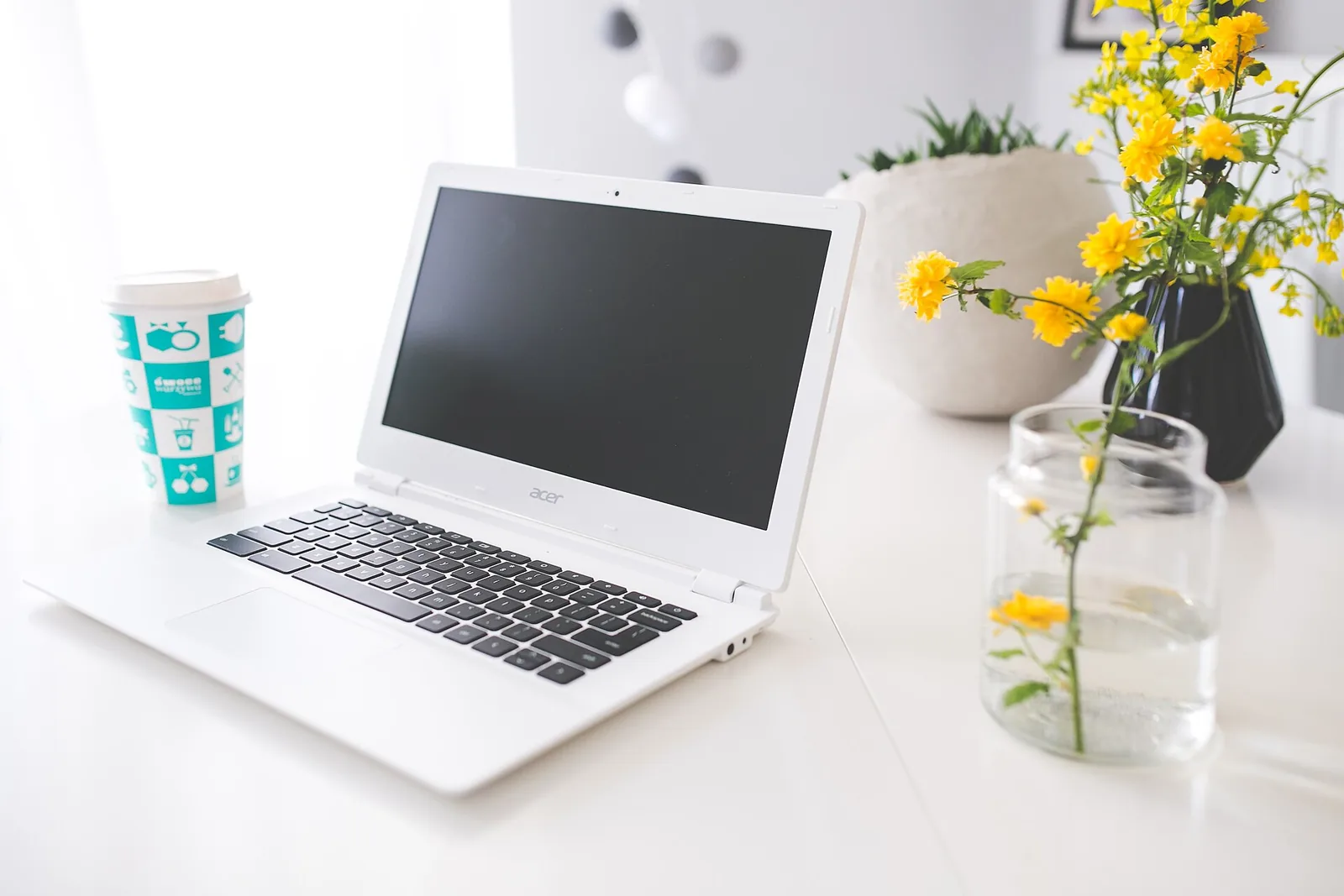A white laptop on a desk beside a vase of yellow flowers
