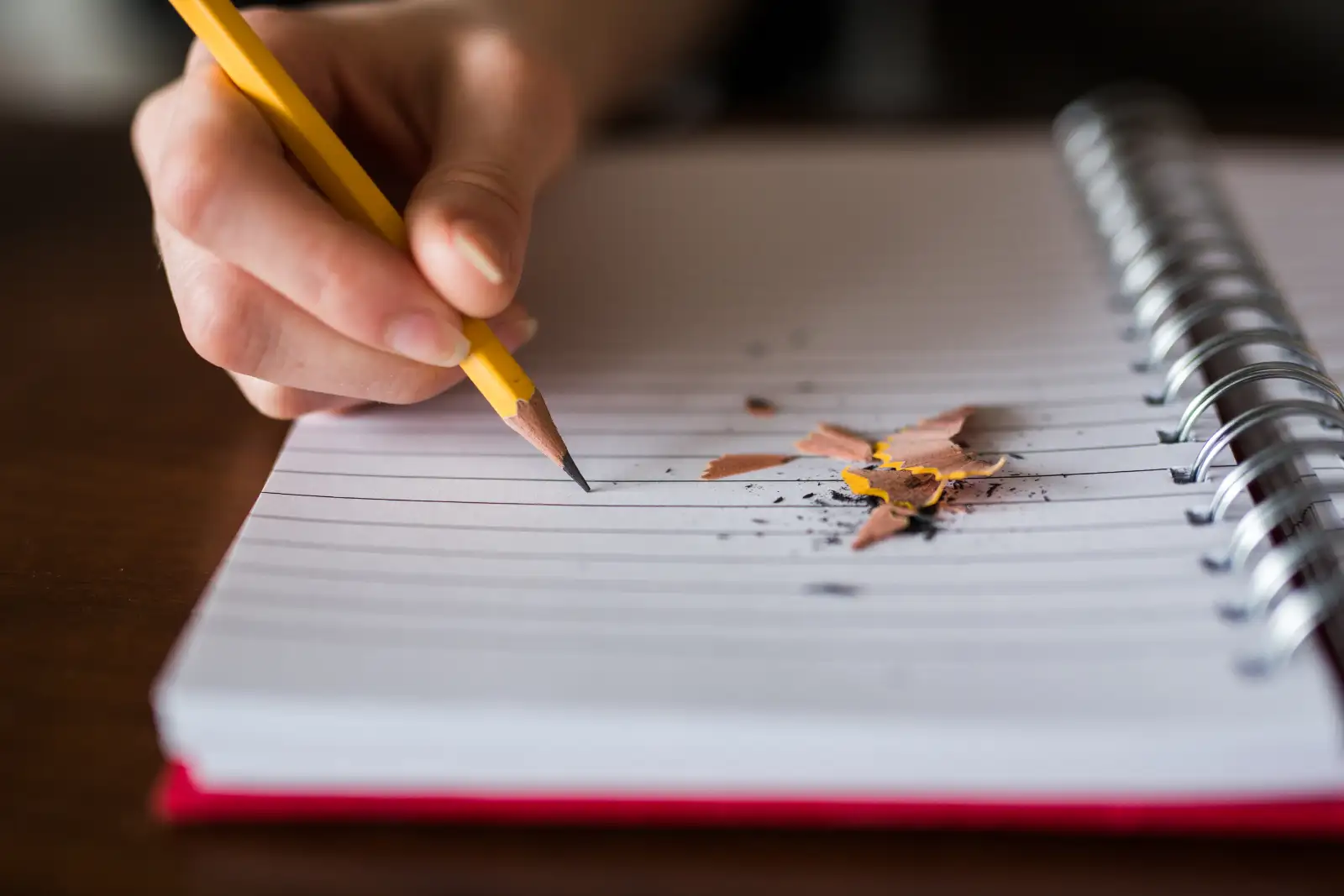 A hand writing in a spiral notebook with a yellow pencil